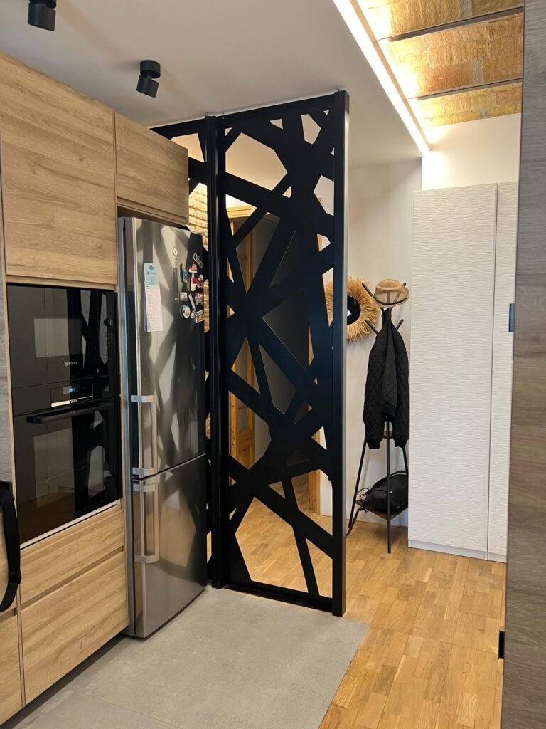 Instalacion de celosía metalica decorativa como separador de ambientes entre una cocina y la entrada de la vivienda, de diseño de rayas entrelazadas lacado en color negro mate en aluminio para Madrid