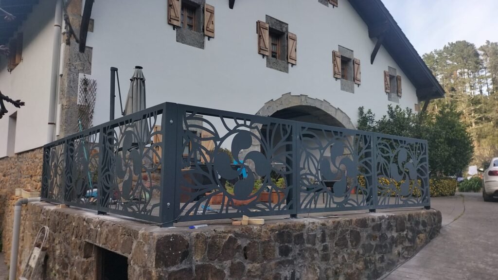 Instalacion de barandilla metalica exterior moderna de diseño especial de un lauburu de Vizcaya, en acero inosidable y lacada al horn en color gris claro para el Pais Vasco