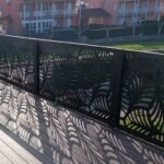 Barandilla metálica de exterior en color negro para terraza con suelo de madera, con diseño botánico de hojas en corte láser proyectando sombras, instalada en Galicia.