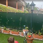 Texto ALT para WordPress (campo 'Texto alternativo'): Panel perimetral de ocultación en acero inoxidable color verde con diseño botánico de naturaleza y mariposas en corte láser, instalado en un jardín exterior en Pontevedra.