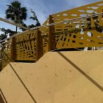 Valla exterior metálica en color mostaza con diseño botánico de hojas en corte láser, instalada sobre un muro divisorio escalonado entre pisos bajos en Málaga.