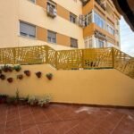 Valla exterior metálica en color mostaza con diseño botánico de hojas en corte láser, instalada sobre un muro divisorio escalonado entre pisos bajos en Málaga.