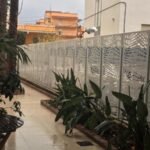 Valla perimetral metálica en color blanco con diseño abstracto en corte láser, instalada junto a jardineras en el pasillo exterior de un hotel en la costa de Valencia.