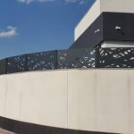 Valla perimetral metálica en color negro con diseño abstracto en corte láser, instalada sobre un muro curvo blanco en el jardín exterior de una vivienda de lujo en Madrid.