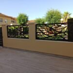 Valla perimetral metálica en color negro con diseño orgánico de ramas en corte láser, instalada sobre un murete exterior para delimitar un recinto privado de piscina en Madrid.