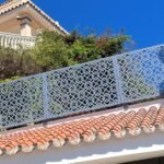 Valla metálica de seguridad en color gris con diseño geométrico en corte láser, instalada sobre un muro exterior con tejas en un chalet independiente en Málaga.
