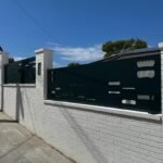 Valla perimetral metálica oscura con diseño exclusivo a medida para el cliente, con aberturas rectangulares minimalistas en corte láser, instalada sobre un muro exterior de ladrillo blanco en una zona de lujo en Barcelona.