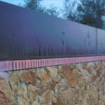 Valla perimetral de aluminio oscuro diseñada para aportar privacidad, con motivos vegetales en corte láser en su base, instalada sobre un muro rústico de piedra y ladrillo en Zaragoza.