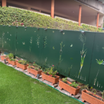 Valla metálica de chapa ciega en acero inoxidable color verde diseñada para ofrecer gran privacidad, con motivos botánicos y mariposas en corte láser en la base, instalada junto a jardineras en un jardín de Pontevedra