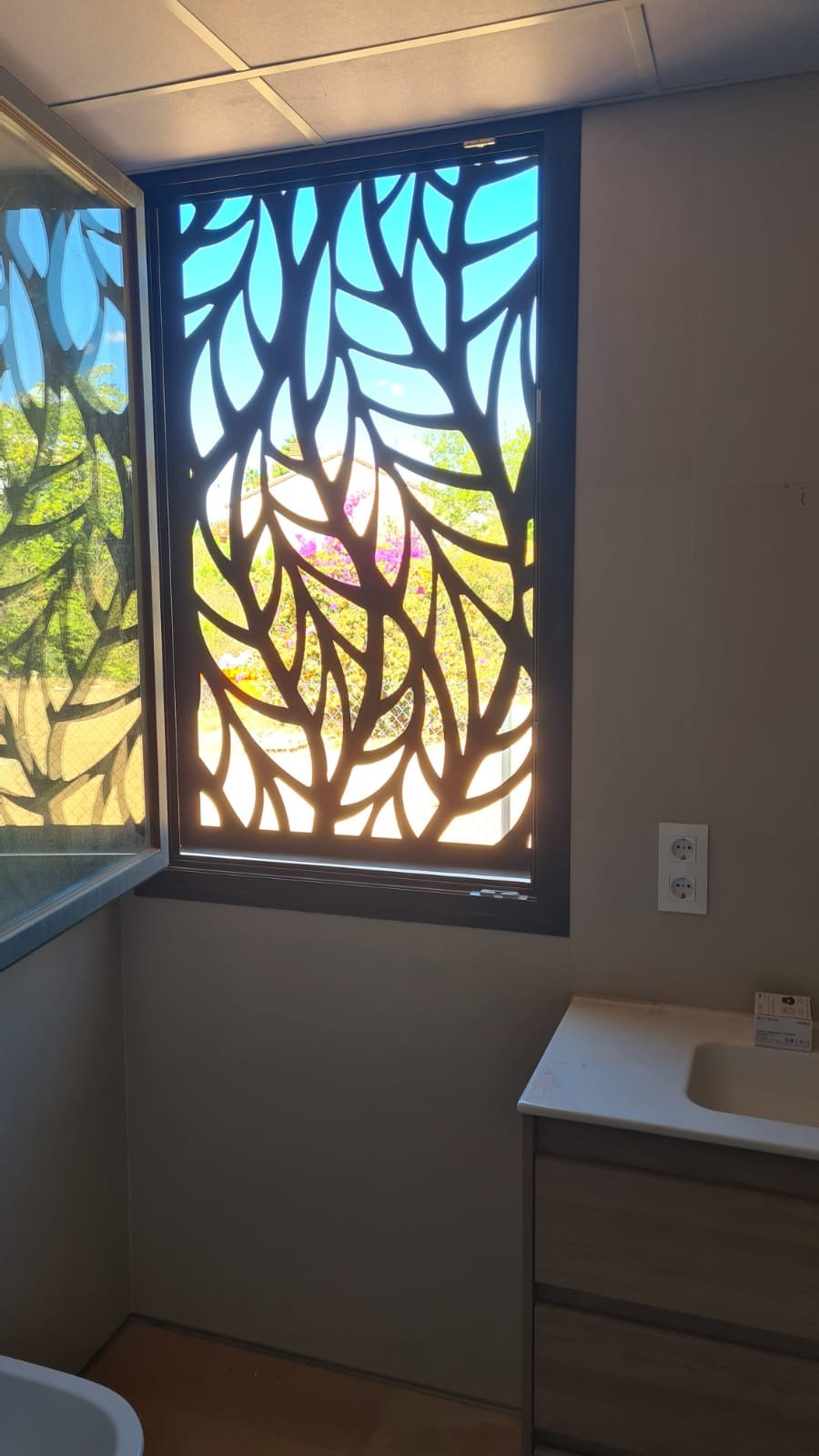 Reja de seguridad y celosía metálica en acero inoxidable en Madrid. Cerramiento exterior decorativo con diseño botánico fabricado a medida mediante corte láser para ventana