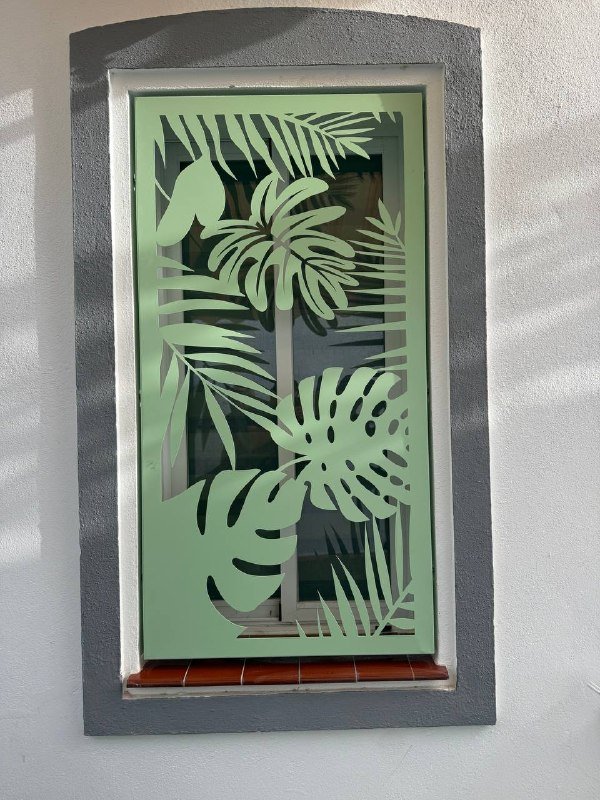 Reja de seguridad y celosía metálica en Coín, Málaga. Diseño personalizado de hojas tropicales en color verde fabricado a medida mediante corte láser para ventana