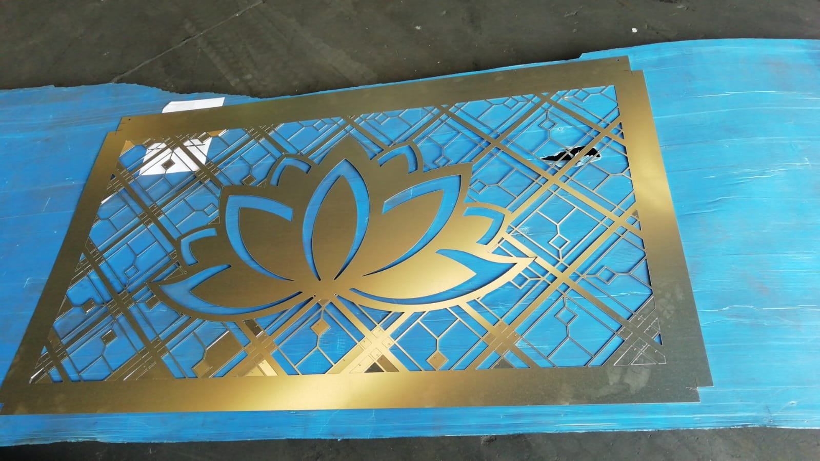 Celosía decorativa de acero mecanizada a medida con patrón geométrico y motivo floral central para revestimiento de pared en dormitorio.