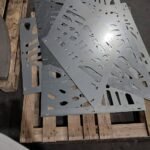 Conjunto de paneles metálicos apilados sobre un palé tras el proceso de corte láser, diseñados con un patrón de huecos irregulares para su instalación como valla sobre muro.